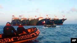Anggota Penjaga Pantai Filipina menggunakan perahu karet saat berpatroli di samping kapal China yang ditambatkan di Whitsun Reef, Laut China Selatan, 14 April 2021. (Foto: AP)