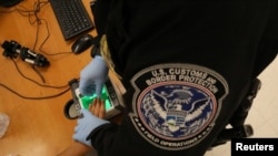 FILE - A woman who is seeking asylum has her fingerprints taken by a U.S. Customs and Border patrol officer at a pedestrian port of entry from Mexico to the United States, in McAllen, Texas, May 10, 2017.