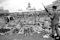 FILE - In this Oct. 6, 1976 file photo, police stand guard over leftist Thai students on a soccer field at Thammasat University, in Bangkok, Thailand. For some Thais, the bloody events of October 6, 1976 are still a nightmare. On that day, heavily armed s