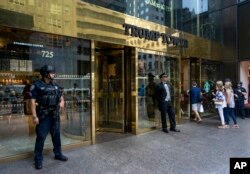 FILE - People pass a police security officer and a building doorman in front of Trump Tower in New York, Aug. 14, 2017. President Donald Trump's bisiness empire will get a closer look this week as his former personal lawyer Michael Cohen tesifies before congressional committees.