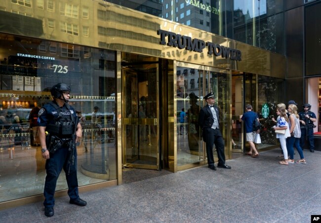 FILE - People pass a police security officer and a building doorman in front of Trump Tower in New York, Aug. 14, 2017. President Donald Trump's bisiness empire will get a closer look this week as his former personal lawyer Michael Cohen tesifies before congressional committees.