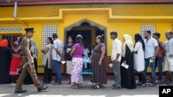 Sri Lankans queue to cast their votes as a police officer stands guard at a polling station during the presidential election in Colombo, Sri Lanka, Nov. 16, 2019.