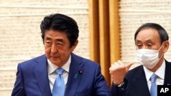 Perdana Menteri Jepang Shinzo Abe, kiri, memberi isyarat saat Kepala Sekretaris Kabinet Yoshihide Suga melihat pada akhir konferensi pers di kantor Abe di Tokyo pada hari Senin, 4 Mei 2020. (Foto: AP)