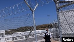 A private security employee stands guard during the inauguration of a closed-type migrant camp on the island of Samos, Greece, Sept. 18, 2021. 