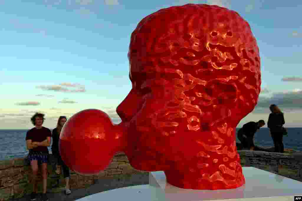 Khách tham quan bên cạnh một tác phẩm điêu khắc hình một cái đầu thổi bong bóng kẹo cao su của nghệ sĩ Qian Sihua, tại cuộc triển lãm ngoài trời cạnh bờ biển mang tên “Sculpture by the Sea” ở Sydney, Australia.