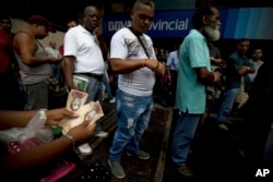 A woman counts her 100-bolivar notes while standing in line outside a bank in Caracas, Venezuela, Tuesday, Dec. 13, 2016.