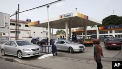 A woman walks past cars buying fuel at a gas station in Lagos, Nigeria, April 24, 2012.
