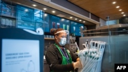 Seorang pegawai Starbucks mengenakan masker sambil menyiapkan pesanan pelanggan di Bandara Ronald Reagan Washington di Arlington, Virginia, 12 Mei 2020.
