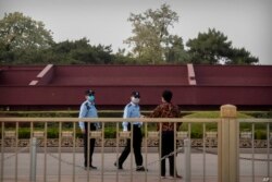 Oficiales de policía chinos usando mascarillas para impedir la propagación del coronavirus hablan con una persona cerca de la Plaza de Tiananmen en Beijing, el 29 de abril de 2020.