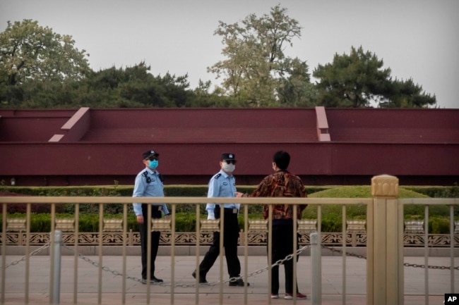 Oficiales de policía chinos usando mascarillas para impedir la propagación del coronavirus hablan con una persona cerca de la Plaza de Tiananmen en Beijing, el 29 de abril de 2020.