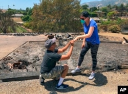 Resident Ishu Rao, on one knee, places this wife's wedding ring on her finger, next to the charred remains of their home in Goleta, Calif., July 8, 2018. The California couple who lost their home in a wildfire made a new happy memory amid the ashes when they found what was left of Laura Rao's wedding ring.