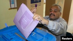 Glasač ubacuje svoj glasački listić i pokazuje prst označen mastilom na glasačkom mestu u Bagdadu
