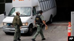 FILE - A van carrying asylum seekers from the border is escorted by security personnel as it arrives at immigration court, in San Diego, California, March 19, 2019.