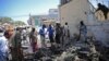 People look at the wreckage of a car bomb outside the Education Ministry in Mogadishu, April 14, 2015. AFP PHOTO / MOHAMMED ABDIWAHAB