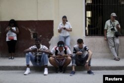 People sit and stand near a Wi-Fi hotspot in Havana, March 17, 2016.