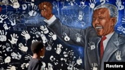 Un muchacho camina frente a un mural pintado en la que fue la casa de Nelson mandela en Johannesburgo. Su estado de salud se ha vuelto delicado.