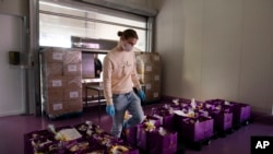 A worker picks orders among bags of chocolate to deliver to a client waiting at a makeshift window at the Chocolate Line warehouse of Dominique Persoone in Bruges, Belgium, Friday, April 10, 2020.