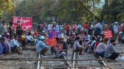 Demonstrators, some holding placards, sit on railway tracks in an attempt to disrupt train service, during a protest against the military coup, in Mandalay, Myanmar, Feb. 17, 2021.