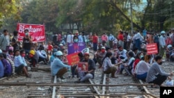 Demonstrators, some holding placards, sit on railway tracks in an attempt to disrupt train service, during a protest against the military coup, in Mandalay, Myanmar, Feb. 17, 2021. 