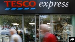 FILE - Tesco, Britain's largest retailer by revenue, plunged to an annual loss of 6.4 billion pounds ($9.5 billion) Wednesday. Pedestrians pass a Tesco shop in London, Sept. 22, 2014. 