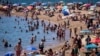 Bañistas se refrescan en el agua mientras otros toman el sol en una playa de Barcelona, España, el 24 de julio de 2024. 