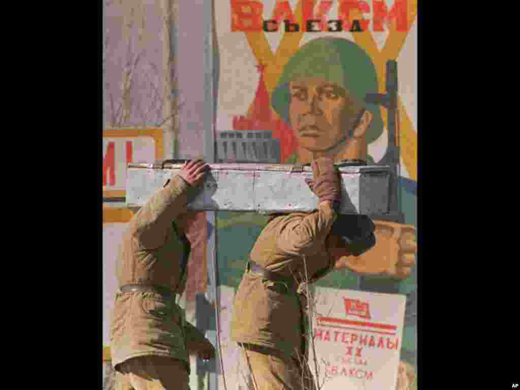 Two Soviet Army soldiers struggle to carry a heavy box full of ammunition past a Soviet military poster at a base in Kabul, Afghanistan, in Jan. 29, 1989. Preparations were underway at the base for the Soviet withdrawal from the region. (AP Photo)