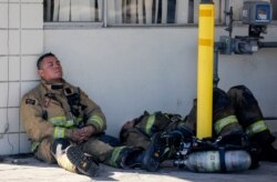 Firefighters rest at outside a cardboard box factory that burned in a wildfire in Riverside, Calif., Oct. 31, 2019. Several blazes broke out in the heavily populated region east of Los Angeles as the Santa Ana winds were predicted to fade.