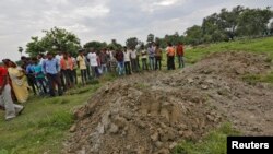 Villagers stand next to mass graves of the school children who died after consuming contaminated meals given to them at a school of the Chapra district, in the eastern Indian state of Bihar, July 18, 2013. 