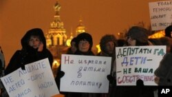 Para aktivis memegang poster bertuliskan "Jangan libatkan anak-anak dalam politik" dan "Pembuat hukum, anak-anak bukan milikmu" dalam protes di St. Petersburg (26/12) atas RUU yang melarang warga AS mengadopsi anak Rusia. (AP/Dmitry Lovetsky)