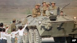 FILE - Afghan children and a soldier bid farewell to Soviet soldiers riding atop an armored personnel carrier as the official troop withdrawal begins after years of military intervention in war-torn Afghanistan on May 15, 1988, in Kabul.