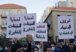 Lebanese anti-government protesters lift placards demanding a stop to economic collapse, transparent elections, and protection of poverty-stricken communities, as they march in a downtown street of the capital Beirut, March 12, 2021.