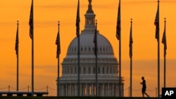 FILE - An early morning pedestrian is silhouetted against sunrise as he walks through the U.S. Flags on the National Mall and past the US Capitol Building in Washington Monday, Nov. 7, 2022, 