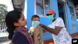 Seorang laki-laki mengenakan masker pada anak kecil di luar Rumah Sakit Pemerintah India, dimana seorang pelajar asal India yang pernah berada di Wuhan diisolasi di Thrissur, negara bagian Kerala, India, 30 Januari 2020. (Foto: AP)