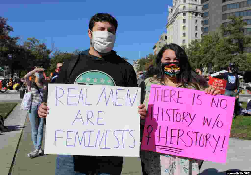 Um homem exibe um cartaz que diz "Homens de verdade são feministas" e o cartaz da senhora diz "Não há história sem a história dela", na Marcha das Mulheres de 17 de outubro. Washington DC