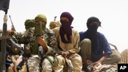 Fighters from Islamist group Ansar Dine stand guard during the handover of a Swiss female hostage for transport by helicopter to neighboring Burkina Faso, at a designated rendezvous point in the desert outside Timbuktu, Mali Tuesday, April 24, 2012. Two m