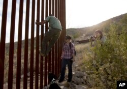 FILE - In this May 11, 2016, photo, former construction foreman Tim Foley shows how to climb a section of the border wall separating Mexico and the United States as journalists Chitose Nakagawa, right, and Marcie Mieko Kagawa look on.