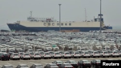 FILE - Newly-manufactured cars and a container ship are seen at Dayaowan port of Dalian, Liaoning province, June 10, 2012. 