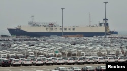FILE - Newly-manufactured cars and a container ship are seen at Dayaowan port of Dalian, Liaoning province, June 10, 2012. 
