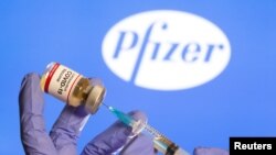 FILE - A woman holds a small bottle labeled with a "Coronavirus COVID-19 Vaccine" sticker and a medical syringe in front of displayed Pfizer logo in this illustration taken, Oct. 30, 2020.