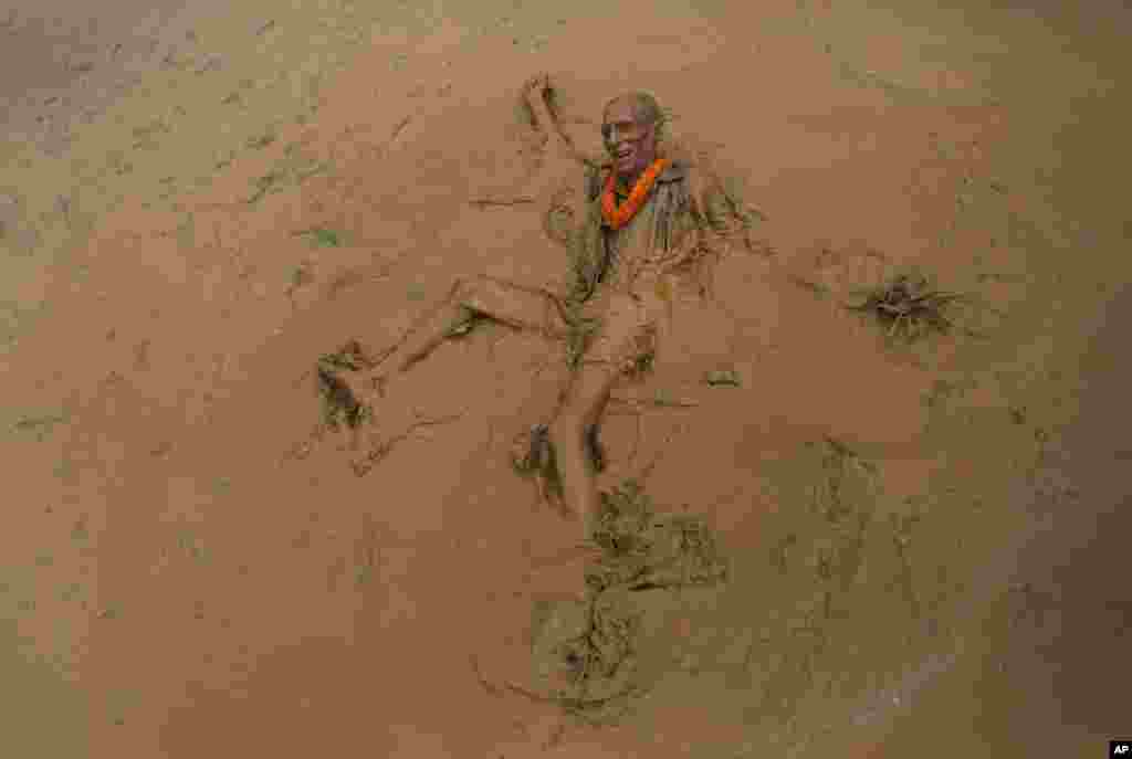 An elderly man falls in the mud in a paddy field during &#39;Asar Pandra&#39;, or paddy plantation day in Dhading district, Nepal.