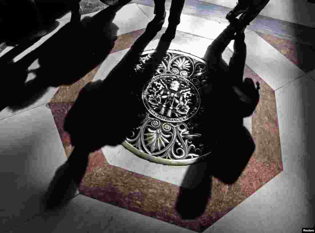 Shadows of tourists are cast across a papal crest dedicated to Pope Pius XII on the floor of Saint Peter's Basilica at the Vatican, March 11, 2013. 