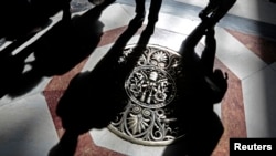 FILE - Shadows of tourists are cast across a papal crest dedicated to Pope Pius XII on the floor of Saint Peter's Basilica at the Vatican, March 11, 2013. 