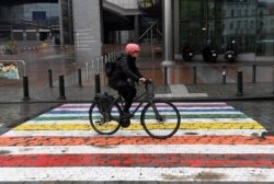 Seorang pengendara sepeda melewati garis penyeberangan jalan (zebra-cross) berwarna pelangi, pada Hari Internasional Melawan Homofobia, Transfobia, dan Bifobia di depan gedung parlemen di Brussel, 17 Mei 2021. (Foto: JOHN THYS / AFP)