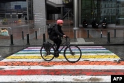 Seorang pengendara sepeda melewati garis penyeberangan jalan (zebra-cross) berwarna pelangi, pada Hari Internasional Melawan Homofobia, Transfobia, dan Bifobia di depan gedung parlemen di Brussel, 17 Mei 2021. (Foto: JOHN THYS / AFP)