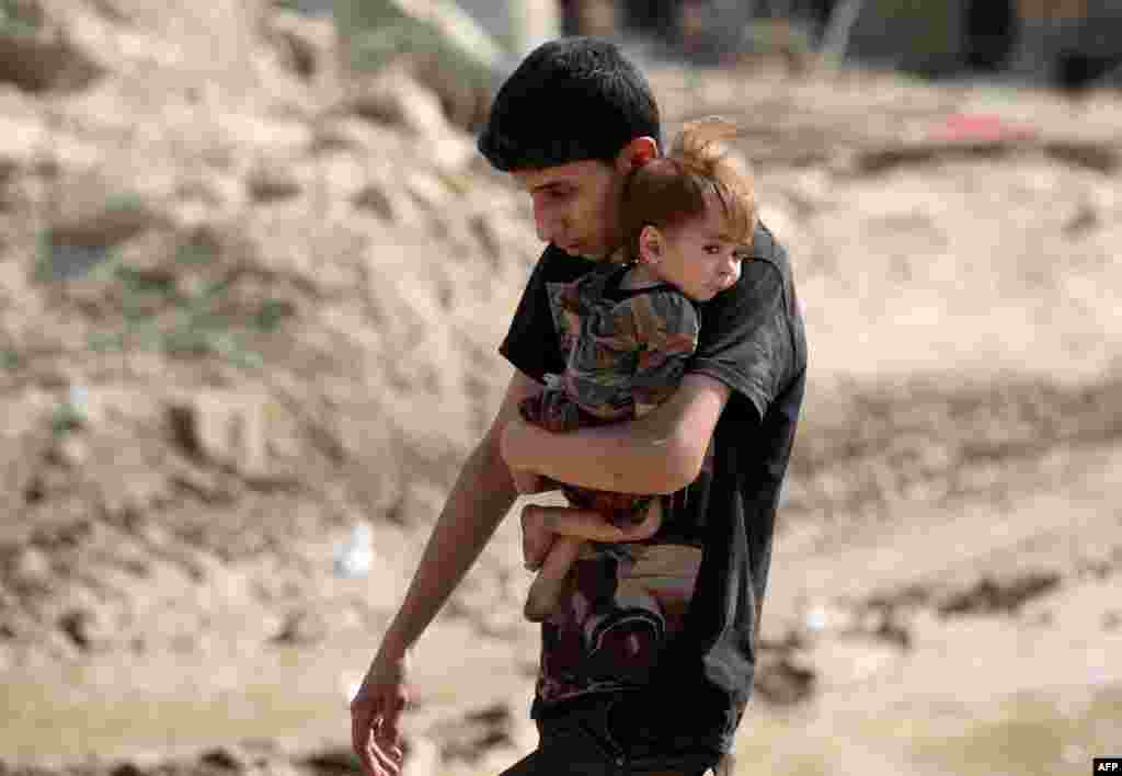An Iraqi youth carries a child while evacuating from the Old City of Mosul, as Iraqi government forces continue their offensive to retake the city from Islamic State (IS) group fighters.