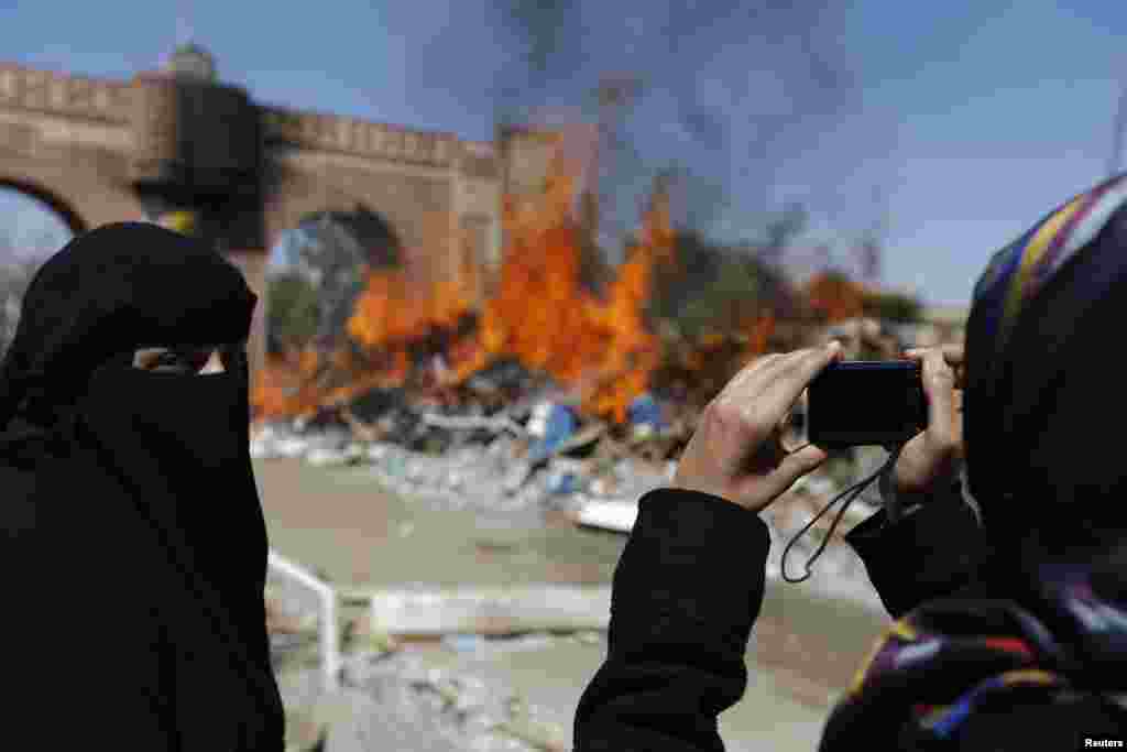 A woman takes a photo of a fire that was set to demolished huts at Taghyeer (Change) Square, where pro-democracy protesters had camped to demand a regime change in 2011, in Sana'a.