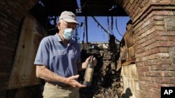 Dario Sattui holds one of the more than 100,000 bottles of wine lost when fire devoured a building near his Tuscan-style castle, Castello di Amorosa in Calistoga, Calif., on Thursday, Oct. 15, 2020. (AP Photo/Eric Risberg)