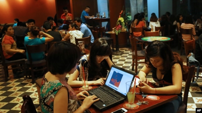 Three young Vietnamese girls use a laptop and smart phones to go online at a cafe in Ha Noi, Viet Nam Wednesday, May 14, 2013. (AP Photo/Na Son Nguyen).