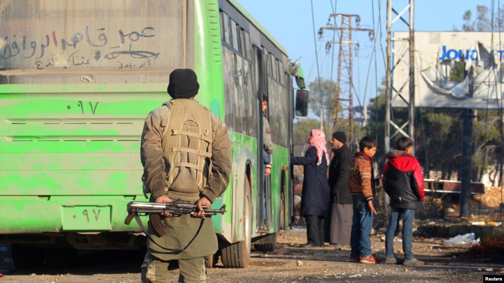 FILE - A rebel fighter stands with his weapon near evacuees from the Shi'ite Muslim villages of al-Foua and Kefraya as they ride buses in insurgent-held al-Rashideen, Syria, Dec. 20, 2016.