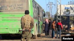 FILE - A rebel fighter stands with his weapon near evacuees from the Shi'ite Muslim villages of al-Foua and Kefraya as they ride buses in insurgent-held al-Rashideen, Syria, Dec. 20, 2016.